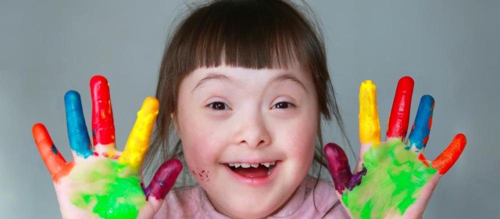 Criança com síndrome de Down sorrindo e com as mão sujas de tinta colorida