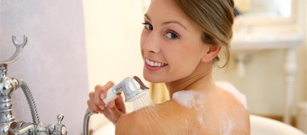 Mulher de costas no banho, segurando uma ducha manual