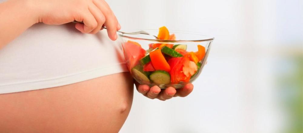 Mulher grávida segurando um pote de salada