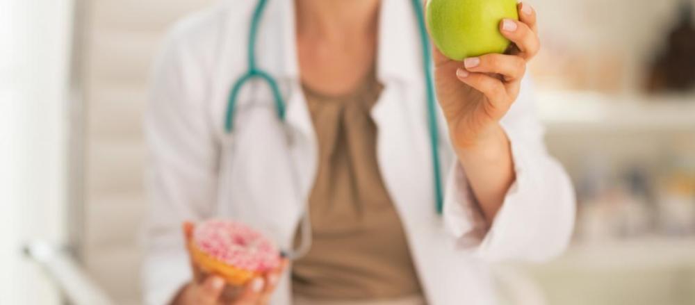 Médica segurando um donut e uma maça verde nas mãos