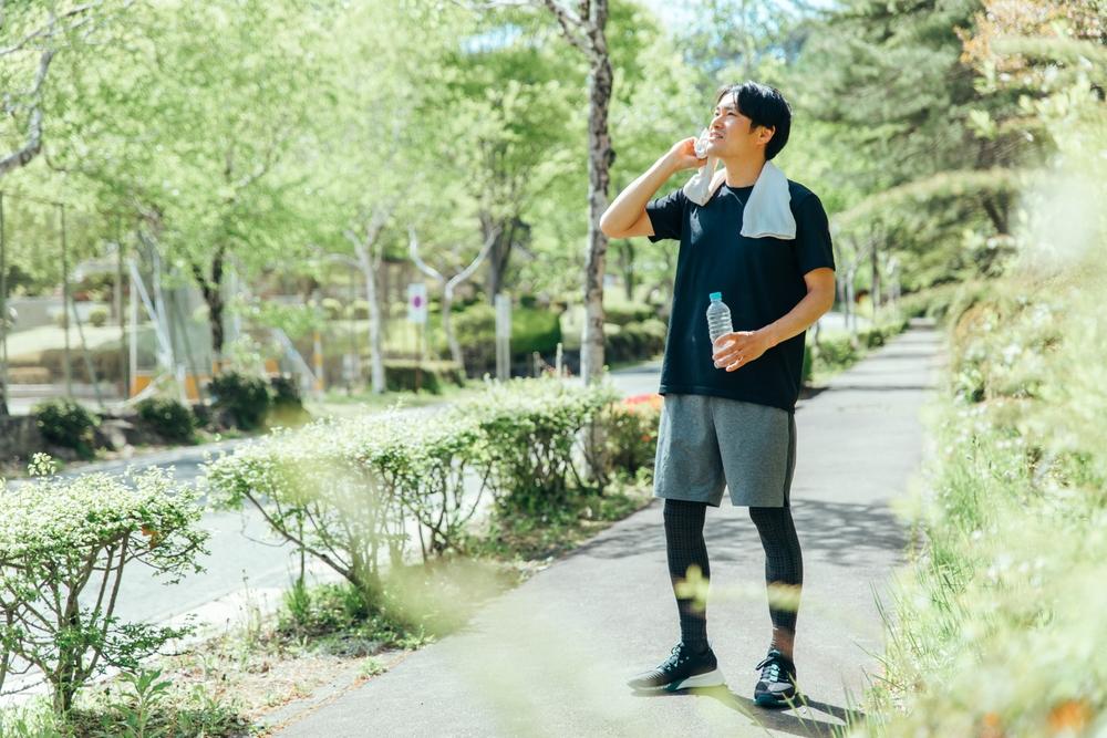 Homem fazendo caminhada ao ar livre com garrafa de água e toalha no ombro, destacando prática regular de atividade física, saúde cardiovascular e benefícios da caminhada diária.