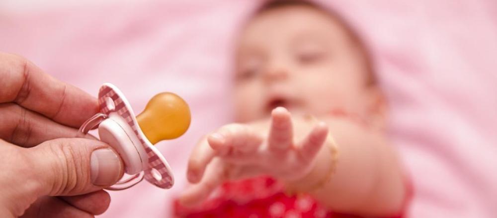 Bebê com as mãos estendidas para pegar chupeta