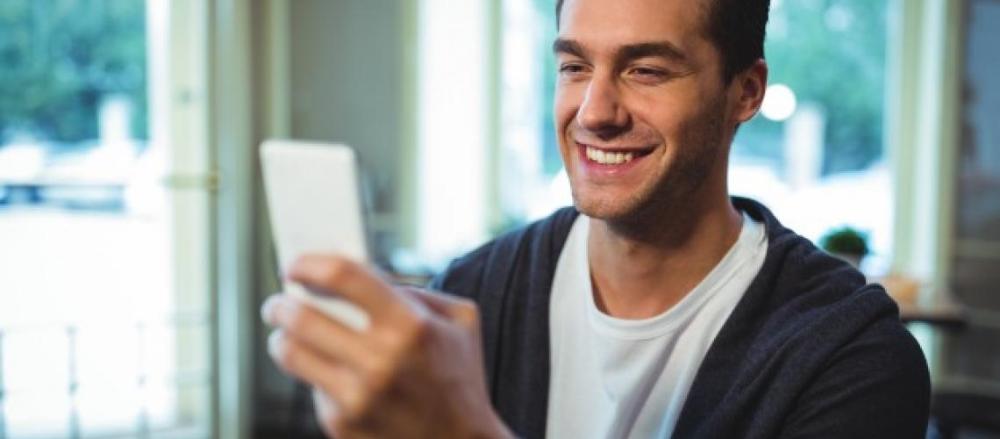 Homem sorrindo enquanto olha para o celular