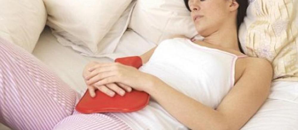 Mulher contendo as dores da mentruação com mbolsa de água quente na barriga