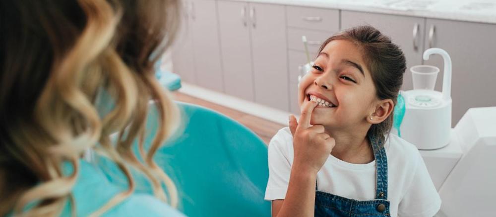 Garotinha sorrindo mostrando os dentes, na cadeira do dentista