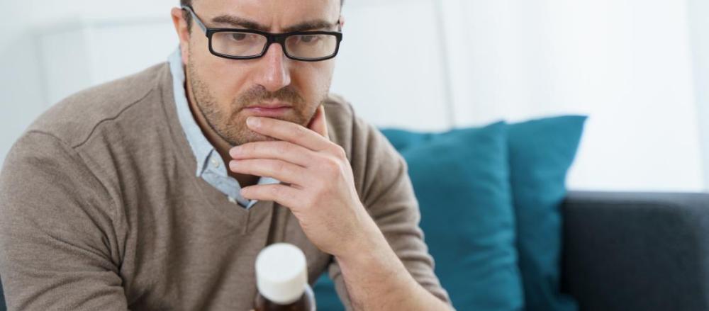Homem observando medicamento, com preocupação