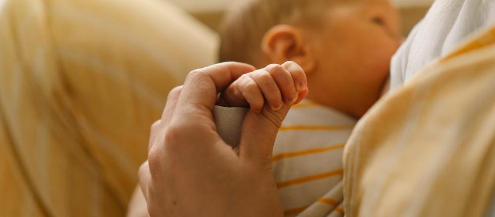 Mãe segurando a mão do bebê enquanto amamenta