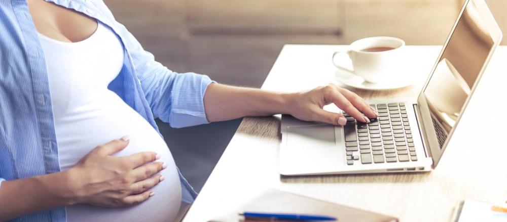 Mulher grávida usando computado com xícara de chá ao lado