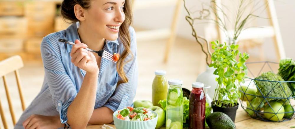 Mulher sorrindo enquanto come alimentos saudáveis como frutas e legumes