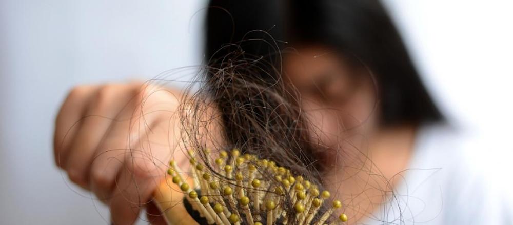 Mulher com expressão negativa segurando uma escova cheia de cabelo 