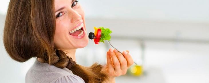 Imagem de uma mulher sorrindo enquanto come salada, simbolizando uma boa mastigação na pós-restauração dentária
