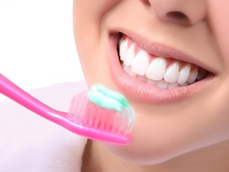 Close de uma boca feminina com uma escova de dentes rosa à frente dela