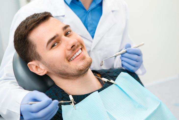 Imagem de um homem sorrindo enquanto está em uma consulta com um dentista