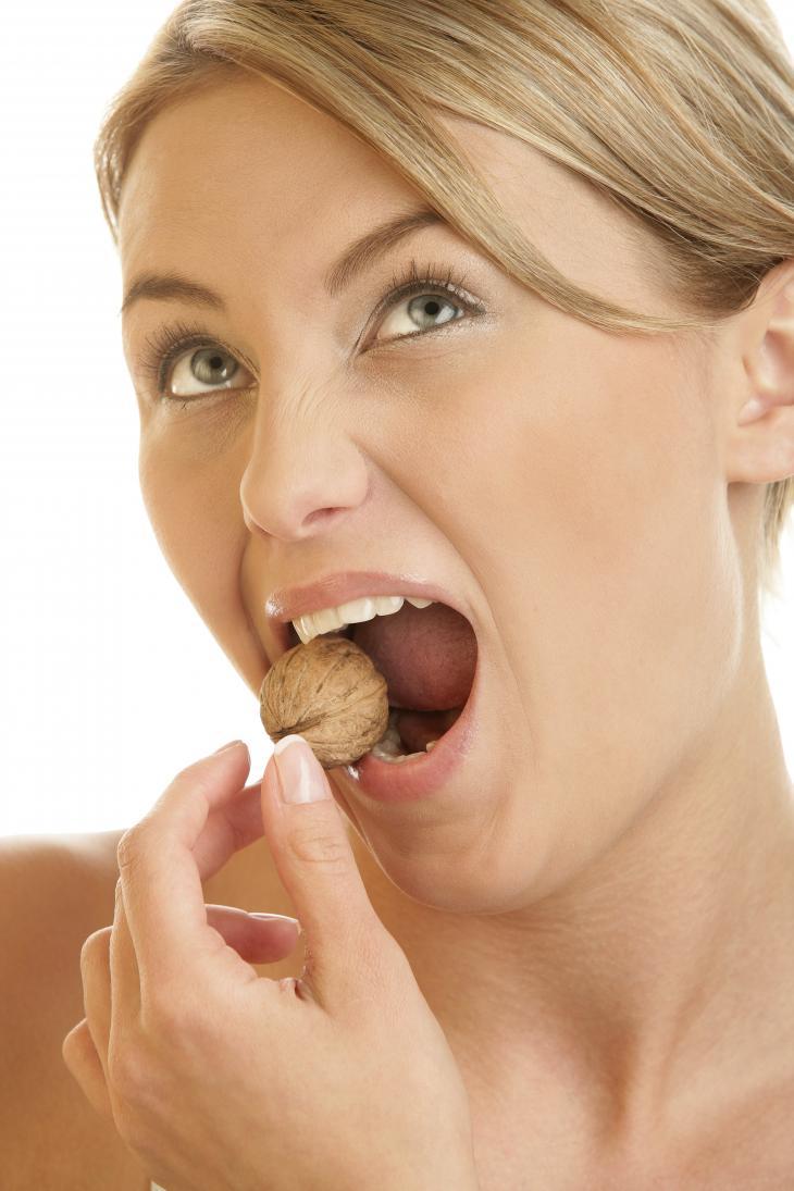 Close do rosto de uma mulher enquanto ela morde uma espécie de castanha ou noz