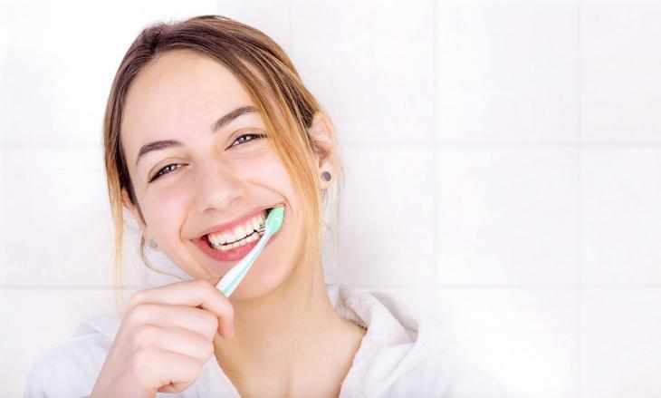 Imagem de uma mulher sorrindo enquanto escova os dentes