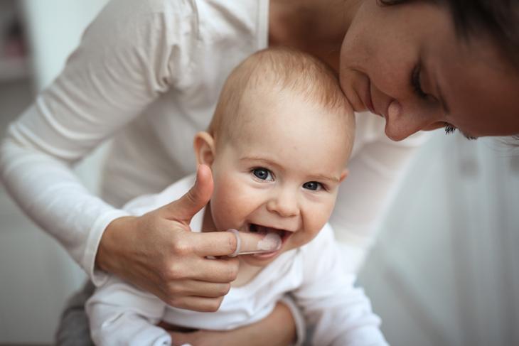 Imagem de uma mãe limpando a boca do bebê com uma dedeira de silicone, simbolizando a higiene bucal nos bebês