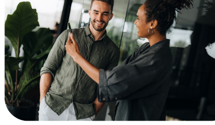 Duas pessoas conversando enquanto olham um celular em ambiente corporativo.