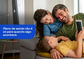 Família sorridente sentada no sofá de casa, transmitindo alegria, união e bem-estar.