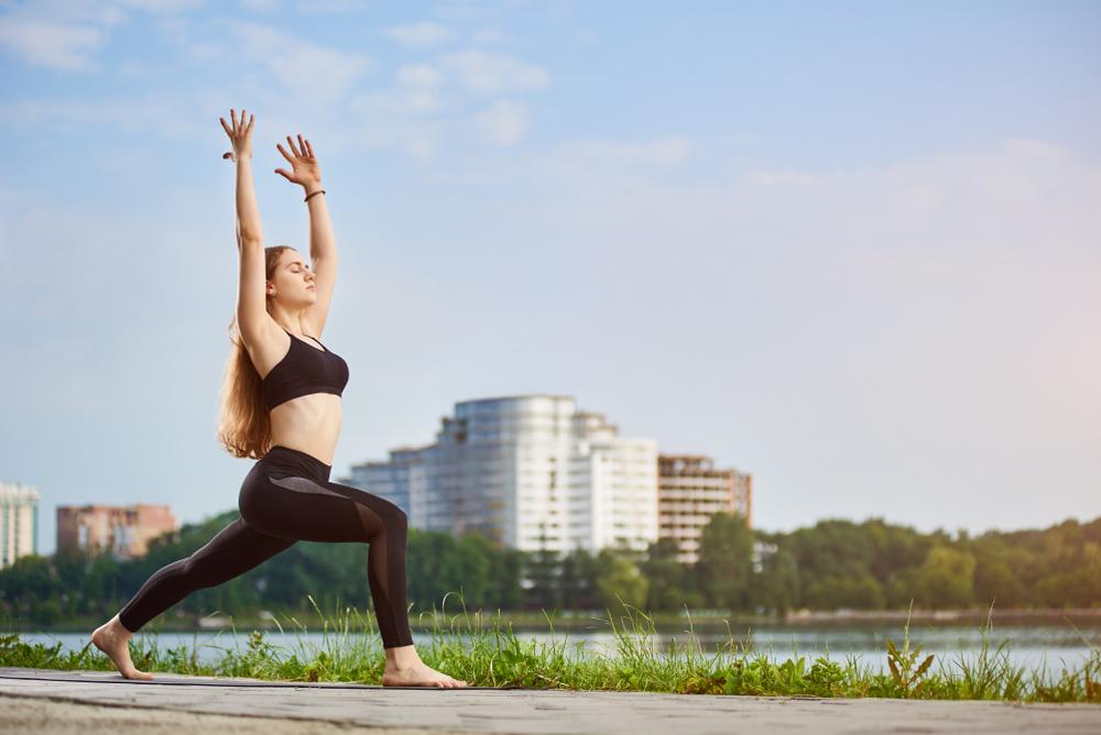 Mulher praticando exercício físico ao ar livre, com postura de alongamento em um parque urbano, representando a adoção de hábitos saudáveis e um estilo de vida ativo.