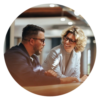 Duas pessoas estão conversando de forma amigável em um ambiente corporativo, demonstrando colaboração e bom relacionamento profissional.