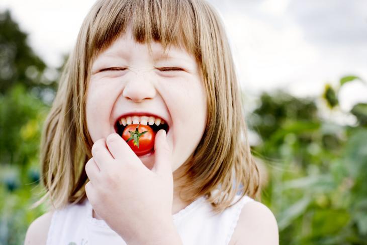 Imagem de uma menina comendo um tomate pequeno