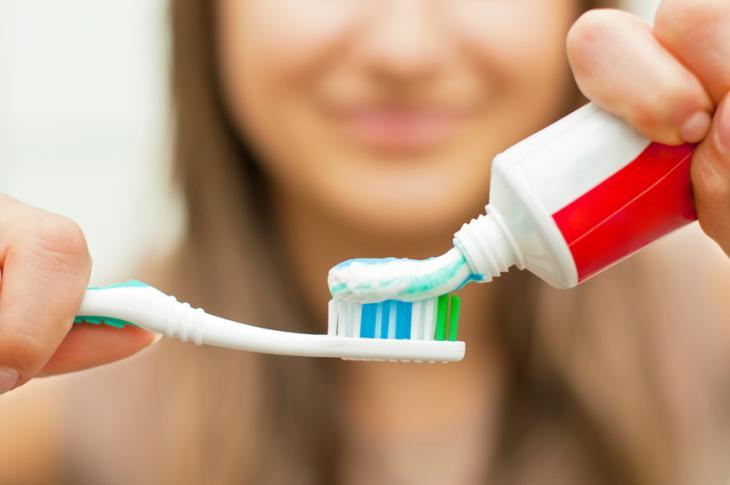 Imagem de uma jovem depositando creme dental na escova de dentes, reforçando importância do flúor na higiene bucal