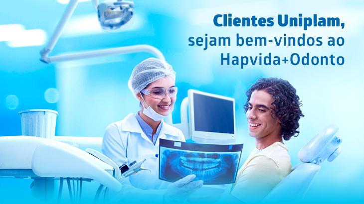 Dentista sorrindo mostra radiografia odontológica a paciente em consultório. Texto dá boas-vindas aos clientes Uniplam ao Hapvida+Odonto