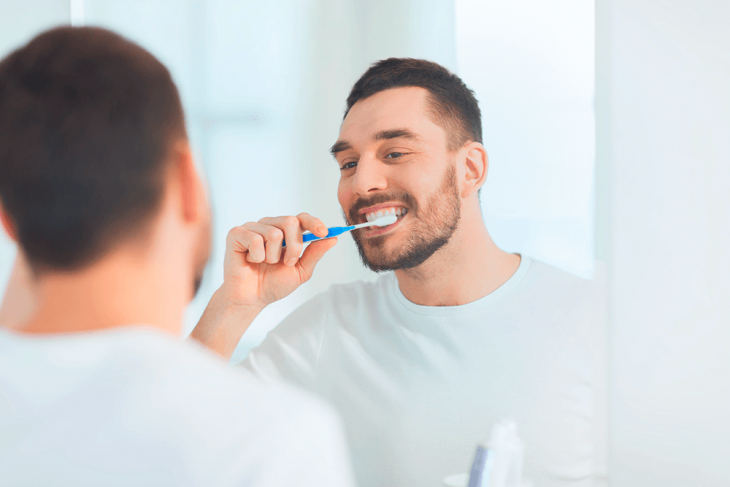 Imagem de um homem escovando os dentes em frente a um espelho