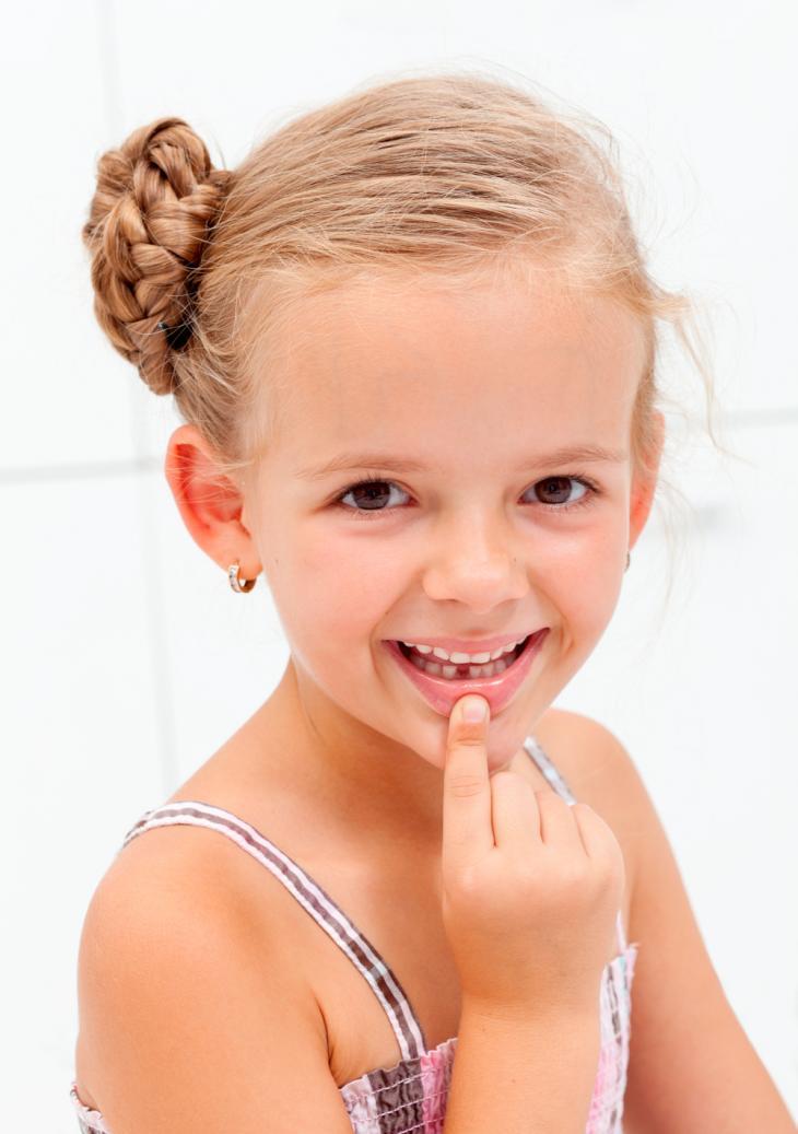 Imagem de uma criança sorrindo e apontando para um dente de leite que caiu