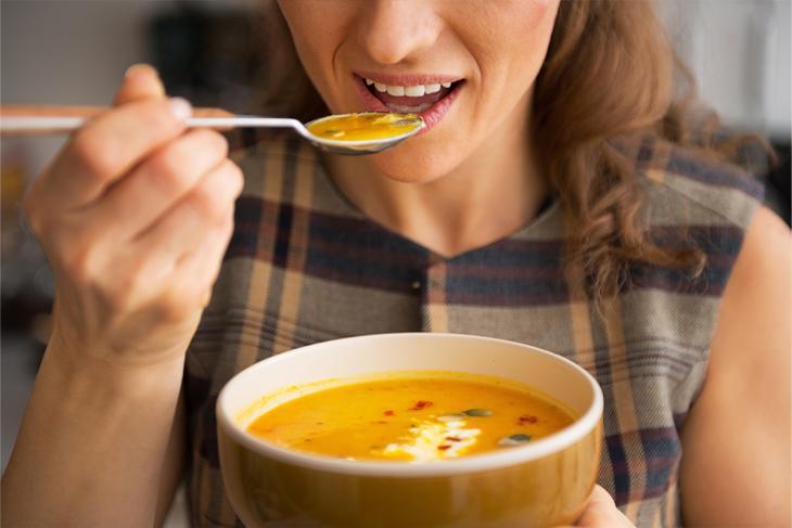 Imagem de uma mulher tomando sopa, um dos alimentos recomendados no pós-operatório da extração do dente do siso 