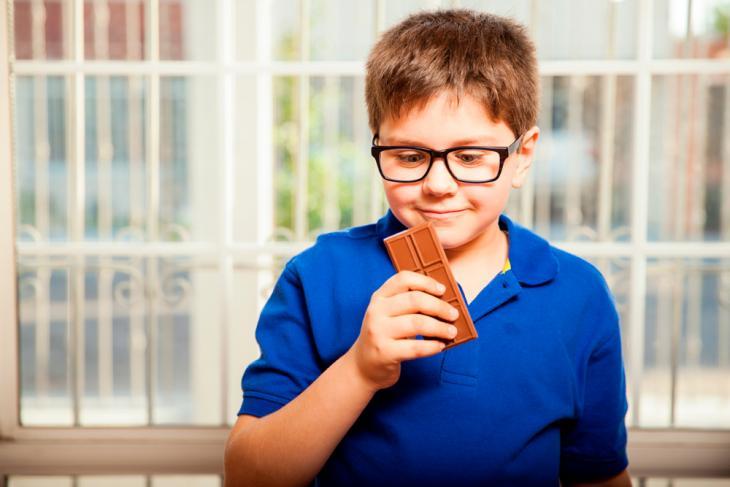 Imagem de um menino segurando uma barra de chocolate, destacando a relação entre o consumo de açúcar e o surgimento de cáries