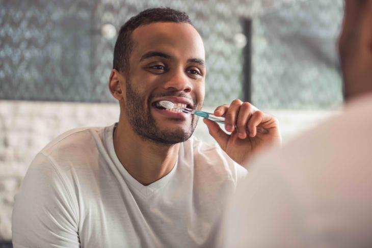 Imagem de um homem escovando os dentes em frente a um espelho