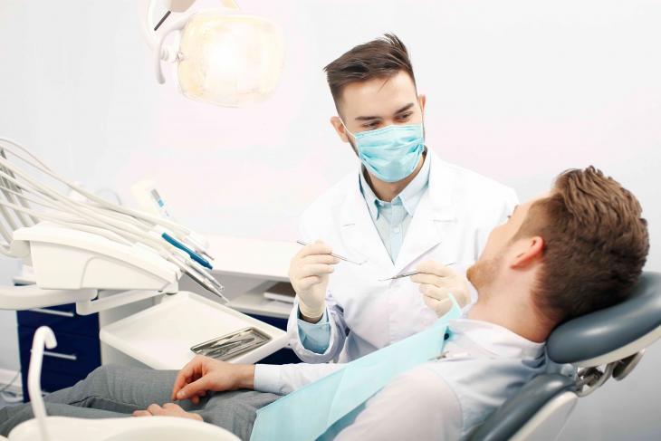 Imagem de paciente em consulta odontológica enquanto dentista realiza check-up. 