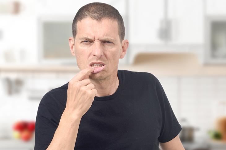 Imagem de um homem com expressão de desconforto tocando os lábios, sugerindo afecções bucais como as aftas